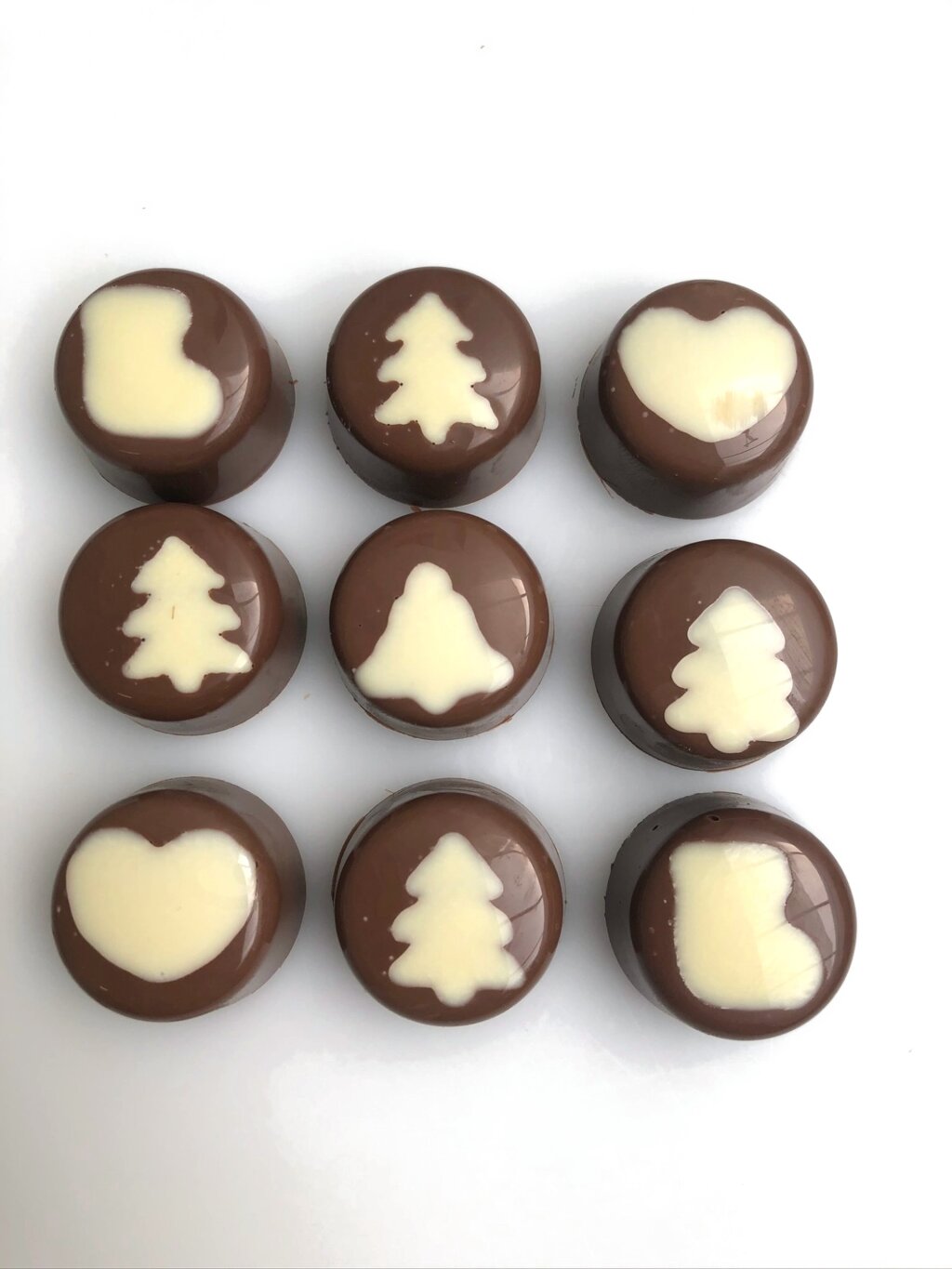 Nine milk chocolate pralines with white Christmas figures: trees, hearts, boots and a bell