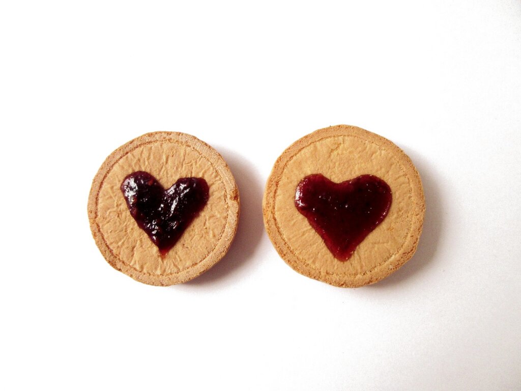 Two round shortbread biscuits, each with a heart of red jam deposited in the centre