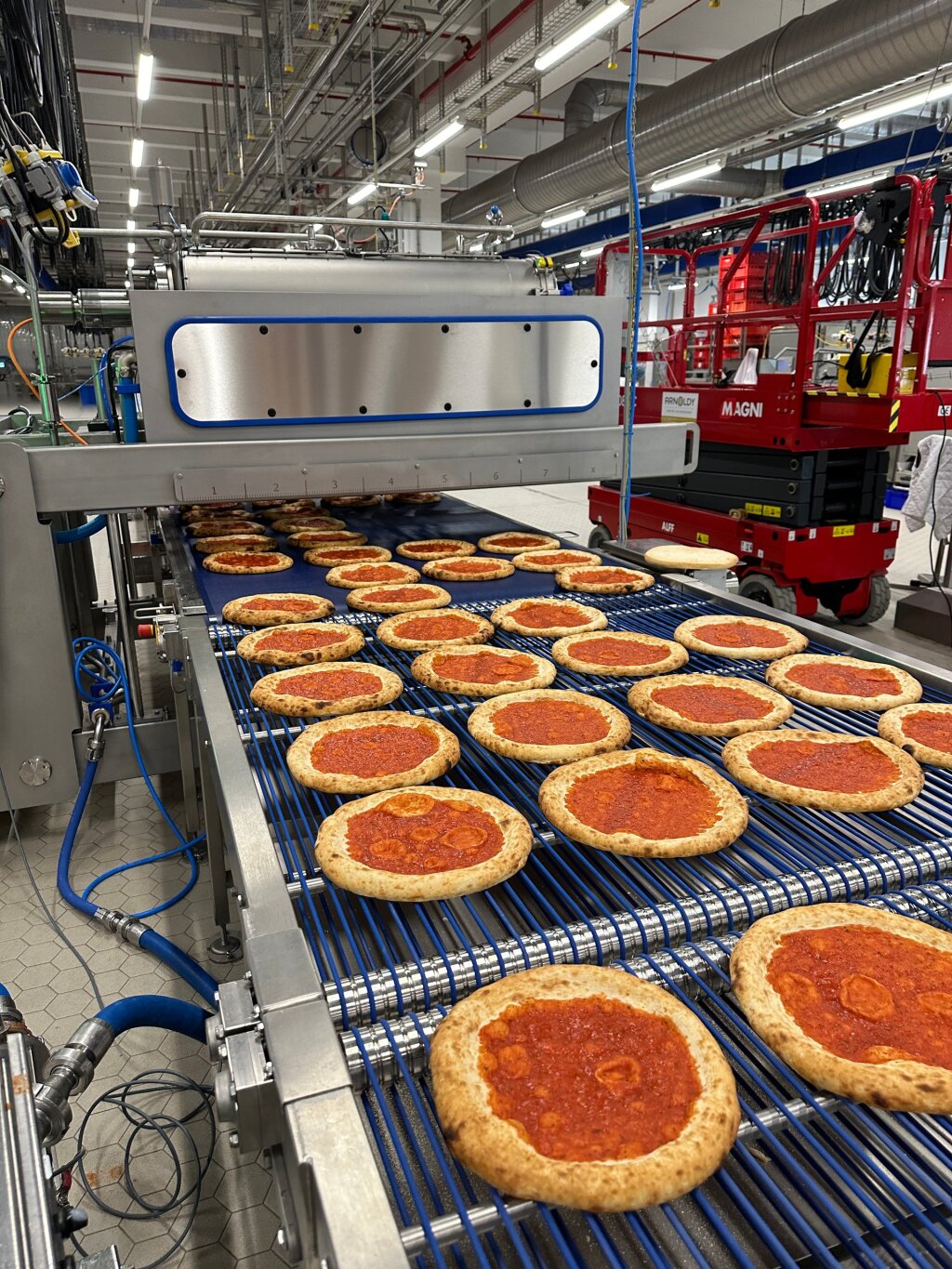 Pizza line in production with sauce on the bases