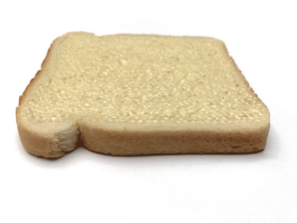 Side view of a slice of white bread with a thin layer of spread on top