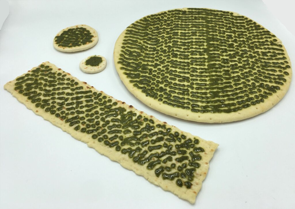 Green pesto in short lines on a large round base, a long flatbread and two small round flatbreads