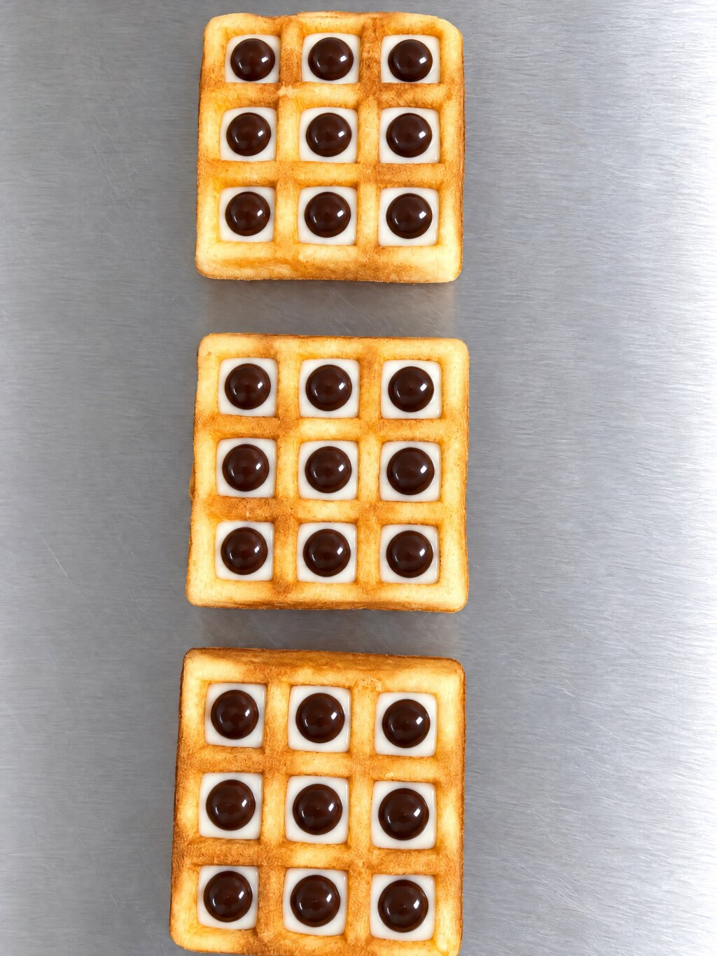 Three square waffles on stainless steel, each cavity with white compound and a drop of dark compound